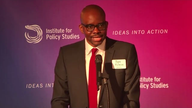 Tope Folarin speaking into a microphone in front of the Institute for Policy Studies backdrop.