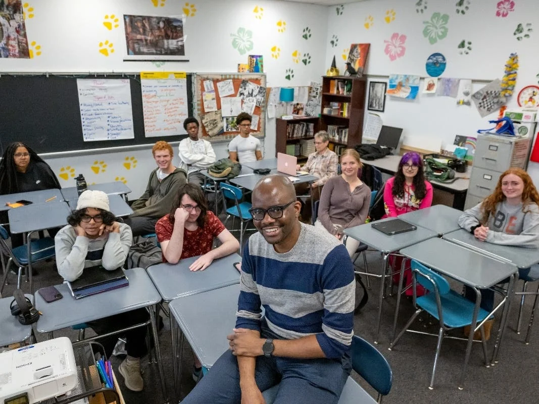 Tope Folarin seated among students in a classroom at Wilde Lake High School.